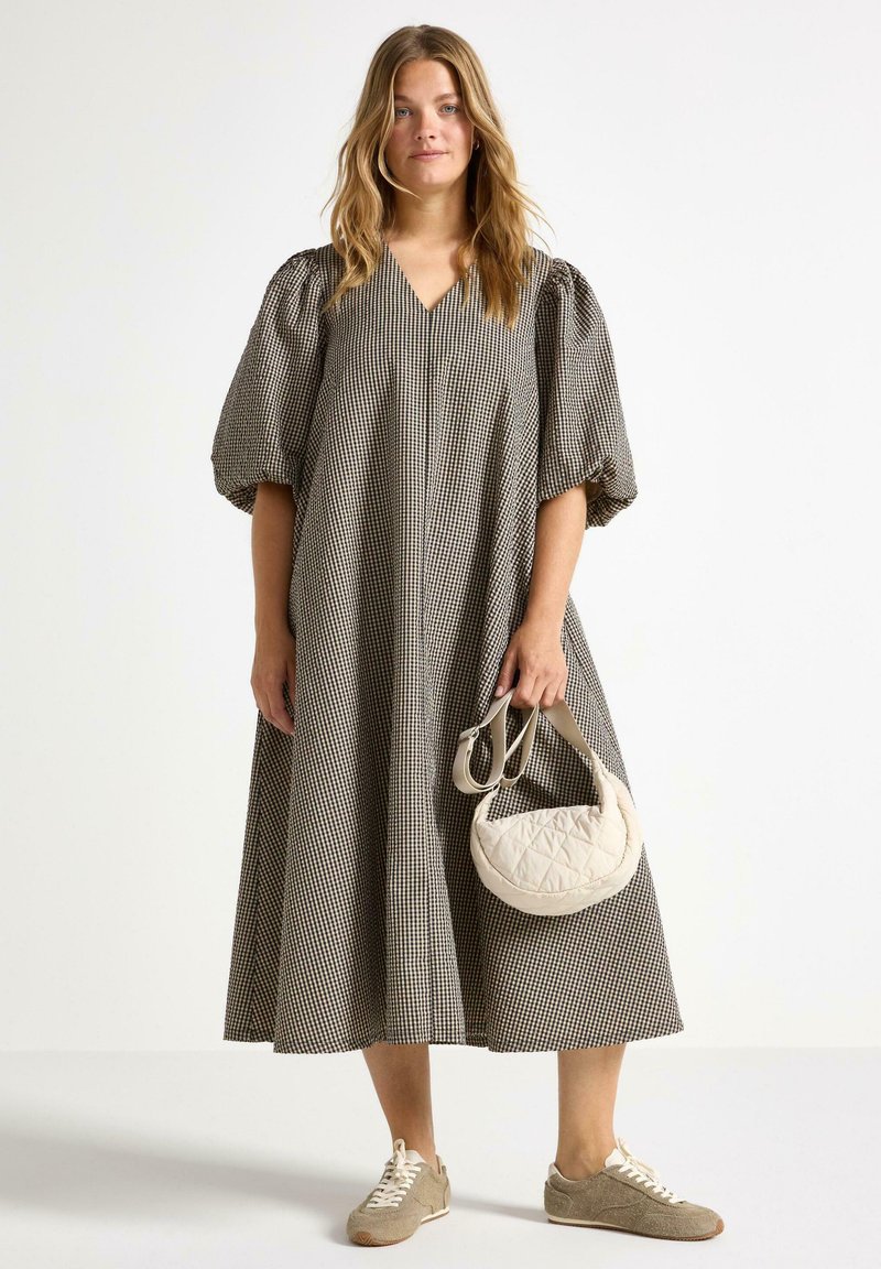 Vestito a scacchi con maniche a palloncino, scollatura a V e silhouette A-line. Abbinato a una borsa in crema trapuntata e scarpe da ginnastica marrone chiaro testurizzate.