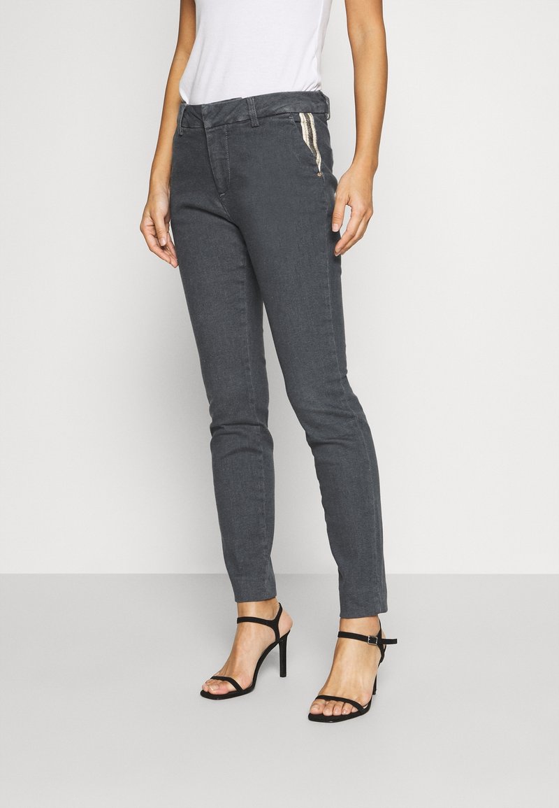 Pantalon structuré gris à coupe slim, avec une texture lisse et deux poches latérales zippées. Porté avec des escarpins noirs à brides.