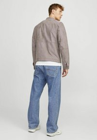 Giacca in suede grigia con collo a sbuffo e polsini a bottoni, abbinata a jeans azzurri larghi e sneaker bianche.