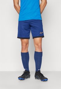 Nike sinised sportlikud lühikesed püksid mustade äärepunnidega, koos siniste põlvepikkuste sokkidega ja mustade jalgpallikleitidega, millel on sinised aktsendid.