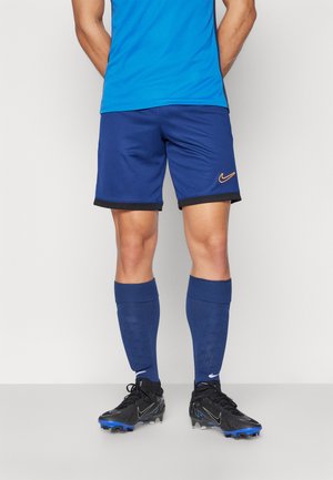 Nike mėlyni sportiniai šortai su juodu apvadu, derinami su mėlynomis iki kelių kojinėmis ir juodais futbolo batais su mėlynais akcentais.