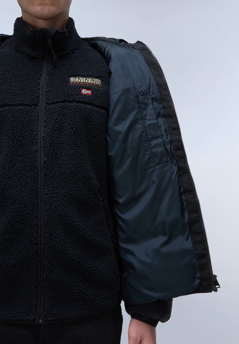 Zwarte fleecajack met gestructureerde textuur, voorzien van een ritssluiting, binnenvoering in marineblauw en geborduurd logo op de linkerborst.