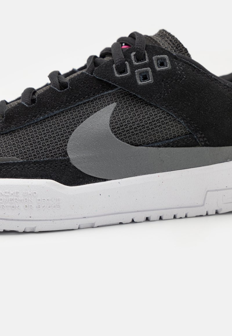 Zapatillas negras hechas de malla y ante con un logo de Nike gris, detalles grises y una suela blanca moteada. Presenta cordones negros y superficie texturizada.