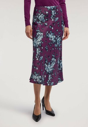 Donna che indossa una gonna midi floreale viola abbinata a una maglia a maniche lunghe viola e a scarpe nere con tacco alto.