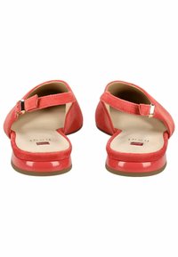 Czerwone zamszowe buty na plecaku z błyszczącym czerwonym obcasem, zaokrąglonym noskiem i regulowanym zapięciem na klamrę. Widoczne miękkie wyściółki wewnętrzne.