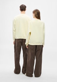 Kremiškai didelio dydžio džemperiai derinami su laisvomis, rudos spalvos korduro keprėmis. Džemperiai turi liemenėlės formos kaklo iškirptę ir rankogalius, kelnės turi galines kišenes.