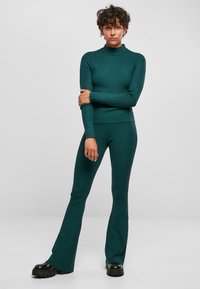 Teal krāsas ribota adīta turtlenecka un atbilstošu platāko bikses komplekts. Pieguļošs dizains ar garām piedurknēm un teksturētu audumu. Melnas apavus ar biezām zolēm.