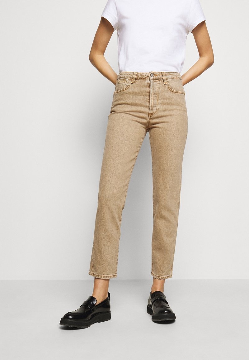 Jeans beige de talle alto en denim claro, con corte recto, cinco bolsillos y sutilezas en las costuras, combinados con mocasines negros.