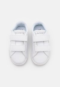 Zapatillas Lacoste blancas con dos correas de velcro, material sintético suave, puntera redondeada y suela texturizada. Nombre de la marca grabado en las correas.