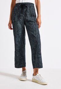 Pantaloni larghi di colore blu scuro con motivo, dotati di una cintura elasticizzata e di un cordoncino. Presentano un design astratto e testurizzato. Abbinati a sneakers bianche.