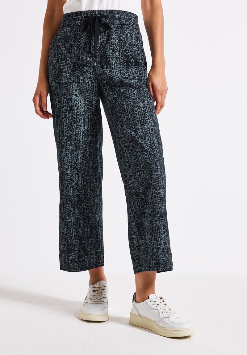 Pantaloni larghi di colore blu scuro con motivo, dotati di una cintura elasticizzata e di un cordoncino. Presentano un design astratto e testurizzato. Abbinati a sneakers bianche.