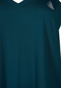Aksamitna koszulka z dekoltem w kształcie litery V w kolorze teal. Posiada subtelny geometryczny wzór na lewym ramieniu. Krótkie rękawy, luźny krój.