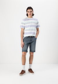 Hvid t-shirt med lyseblå og grå vandrette striber, kombineret med blå denimshorts og brune sko, samt hvide ankelstrømper.