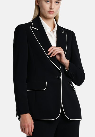 Blazer nero con piping bianco, chiusura a un bottone, due tasche frontali, maniche lunghe e vestibilità sartoriale. Tessuto dal tocco liscio.