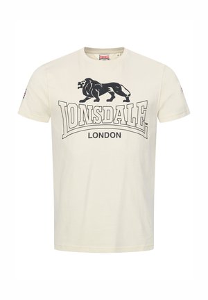 T-shirt color crema in cotone. Presenta una grafica di un leone nero e il testo "LONSDALE LONDON" in grassetto. Maniche corte e design a girocollo.