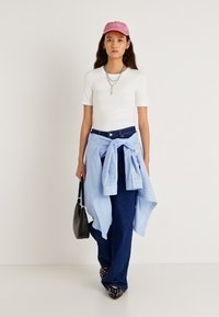 Λευκό κοντομάνικο μπλουζάκι, μπλε ριγέ πουκάμισο δεμένο στη μέση, φαρδιά τζιν παντελόνια, ροζ καπέλο, μαύρη τσάντα, παπούτσια με σχήμα slip-on με βούλες.