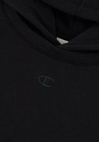 Hoodie noir en tissu doux, avec un col côtelé et un logo brodé discret sur la poitrine. Texture lisse, design minimal.