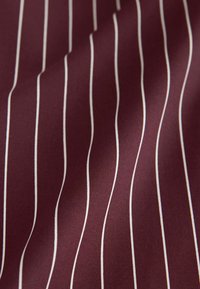 Tissu bordeaux avec fines rayures verticales blanches, légèrement froissé, montrant la texture et la continuité du motif.