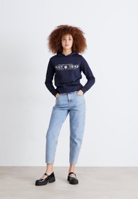 Hanorac bleumarin cu text grafic, blugi ușor spălați, cu croială îngustă, și pantofi cu platformă negri. Material neted, croială lejeră și design cu glugă.