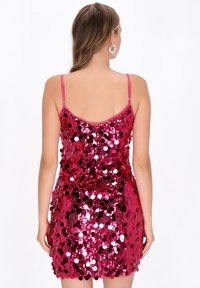 Rózsaszín flitteres miniruha vékony, állítható pántokkal, testhezálló sziluettel és fényes, tükröződő felülettel.