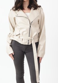 Roomkleurig faux leren jack met een ritssluiting aan de voorkant, een ceintuur in de taille, brede rever en lange mouwen, gecombineerd met donkere spijkerbroeken.