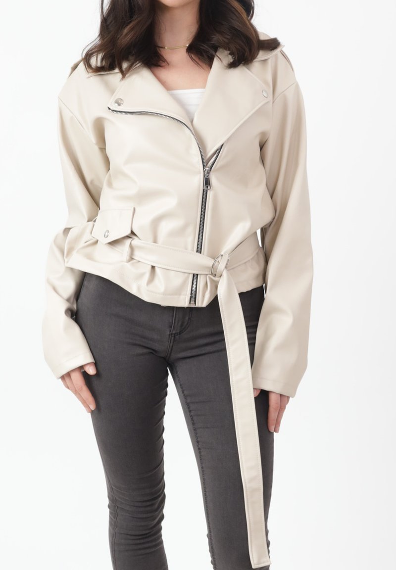 Roomkleurig faux leren jack met een ritssluiting aan de voorkant, een ceintuur in de taille, brede rever en lange mouwen, gecombineerd met donkere spijkerbroeken.