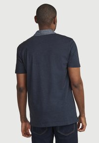 Marineblaues T-Shirt mit kurzen Ärmeln und einem kontrastierenden Denim-Kragen, weicher Textur und leicht abgerundetem Saum, getragen mit dunklen Jeans.