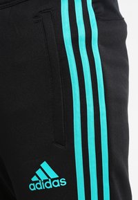 Schwarze Sporthosen mit drei türkisfarbenen Streifen an der Seite. Zu den Merkmalen gehören ein elastischer Bund und ein türkisfarbenes Adidas-Logo in der Nähe des Saums.