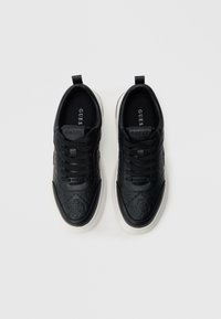 Mustad tennised, mis on valmistatud tekstuurse sünteetilise materjali ja valge kummist tallaga, millel on reljeefsed mustrid ja mustad paelad.