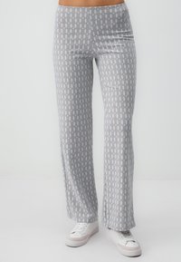 Pantalons larges à motifs gris avec une texture douce, présentant un design répétitif bleu clair et marron. Associés à des baskets blanches.