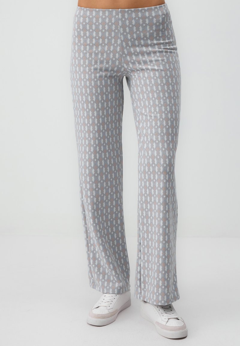 Pantalons larges à motifs gris avec une texture douce, présentant un design répétitif bleu clair et marron. Associés à des baskets blanches.