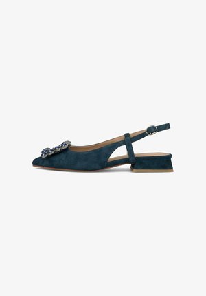 Zapato plano de ante verde azulado oscuro con tiras traseras, tacón bajo de bloque y gran adorno decorativo azul y plateado en la punta puntiaguda.