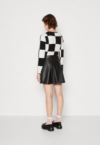 Haut à manches longues à carreaux noirs et blancs, assorti à une jupe évasée en cuir noir. Chaussures noires à semelles épaisses avec des chaussettes visibles, soulignées de rose.