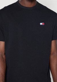 Czarna bawełniana koszulka z krótkim rękawem, z małym haftowanym logo na piersiach w kolorach czerwonym, białym i niebieskim. Okrągły dekolt.