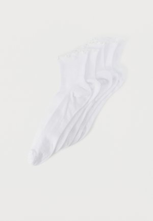Cinq paires de chaussettes blanches pour chevilles avec des bordures à volants empilées sur un fond blanc uni.