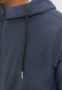 Sudadera con cremallera azul marino de textura suave, con un cordón negro y un regulador de metal. Primer plano del cuello y los detalles de la cremallera.