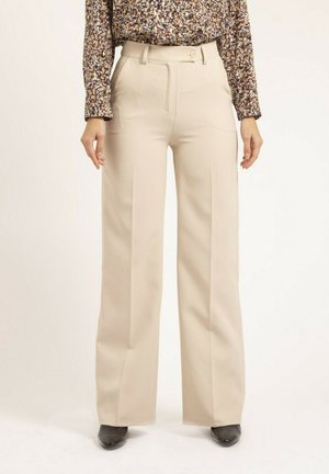 Pantalons beige à jambe large avec une taille haute, des détails plissés à l'avant et un tissu lisse. Portés avec un chemisier à manches longues à motifs.
