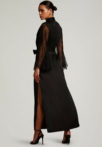 Abito nero con maniche lunghe in pizzo, alta spaccatura, finitura in satin e una cintura in tessuto in vita. Silhouette slanciata con dettagli eleganti.