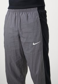 Gray and black lightweight Nike pants with an elastic waistband, side pockets, and a prominent white Nike logo on the left thigh.