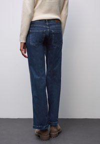 Mörkblå denimjeans med avslappnad passform, med bakfickor och medelhög midja. Matchat med en beige stickad topp och bruna skor.
