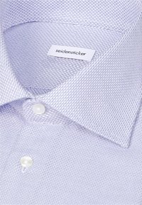 Gros plan sur le col d'une chemise habillée texturée bleu clair avec des boutons blancs et une étiquette de marque Seidensticker à l'intérieur.