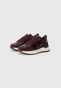 Un paio di sneakers lucide di un intenso borgogna scuro con dettagli in suede e suole spesse color crema, viste da un angolo su uno sfondo chiaro.
