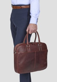 Braune Leder-Laptoptasche mit doppelten Griffen, glatter Textur und Reißverschluss, sichtbar genäht und mit einer Fronttasche.