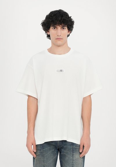 T-shirt en coton blanc oversize à col rond et manches courtes, avec une petite impression graphique sur la poitrine gauche.