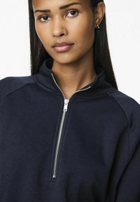 Felpa blu navy con zip e collo alto, dotata di zip argentata, texture morbida e maniche raglan per una vestibilità rilassata.