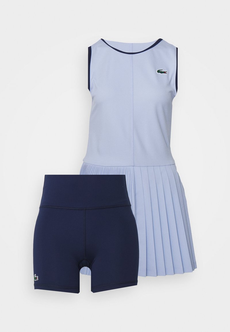 Himmelblaues ärmelloses Tennisdress mit maritimen Akzenten und plissiertem Rock, kombiniert mit navyblauen hoch taillierten Sportshorts mit Logo-Details.