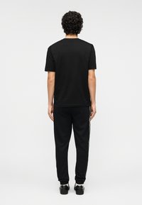 Μαύρο βαμβακερό T-shirt με κοντά μανίκια, συνδυασμένο με μαύρο φούτερ παντελόνι με πλαϊνές ρίγες. Απλός σχεδιασμός, άνετη εφαρμογή και μονόχρωμο.