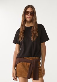 Czarna bawełniana koszulka z krótkim rękawem, zestawiona z brązową zamszową mini spódnicą z szerokim materiałowym paskiem zawiązanym w talii.