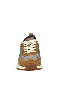 Bruine sneaker met groene accenten, gemaakt van suede en gaas, met witte veters en een rubberen zool met een hexagonaal patroon.