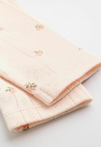 Ljusrosa stickat tyg med små blommönster och delikata perforerade mönster, vikt på en vit yta.
